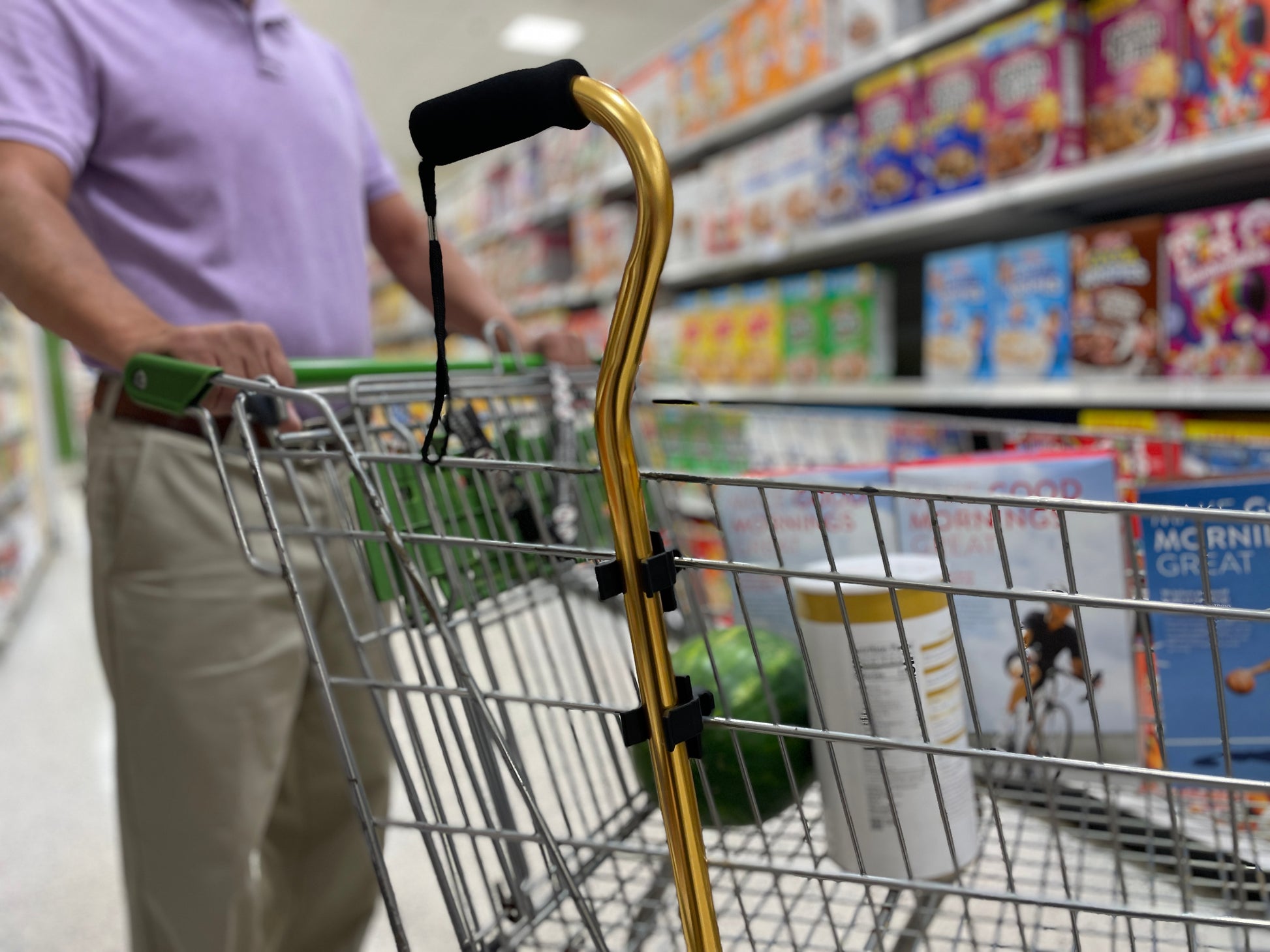 man grocery shopping with gold cane on side of cart